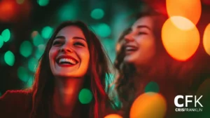 Duas pessoas sorridentes com luzes coloridas desfocadas ao fundo.