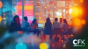 Um grupo de oito pessoas está sentado ao redor de uma mesa em um escritório bem iluminado, com luzes coloridas da cidade visíveis através de grandes janelas.