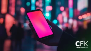 Uma mão segura um smartphone com uma tela rosa brilhante, em contraste com uma paisagem urbana desfocada com luzes coloridas.