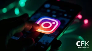 O dedo de uma pessoa tocando o ícone do aplicativo Instagram em uma tela de smartphone, com iluminação colorida e o logotipo CFK CrispFranklin no canto.