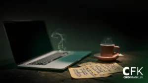 Um laptop, uma xícara de café fumegante em um pires e anotações escritas à mão estão sobre uma superfície de madeira com o logotipo "CFK CRISFRANKLIN" no canto inferior direito.