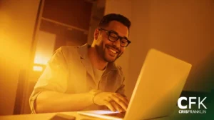 Um homem de óculos sorri enquanto usa um laptop em uma sala com iluminação quente. O logotipo "CFK CRISFRANKLIN" aparece no canto inferior direito.