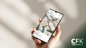 Uma mão segura um smartphone exibindo um perfil do Instagram com um layout de grade minimalista, com imagens em tons neutros. O logotipo "CFK CRISFRANKLIN" aparece no canto inferior direito.