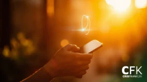 Uma pessoa segura e usa um smartphone ao ar livre com a luz do sol e um efeito de redemoinho brilhante acima do dispositivo; CFK e CRISFRANKLIN são visíveis no canto.